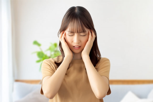 両手でこめかみを押さえ、頭痛をこらえる女性